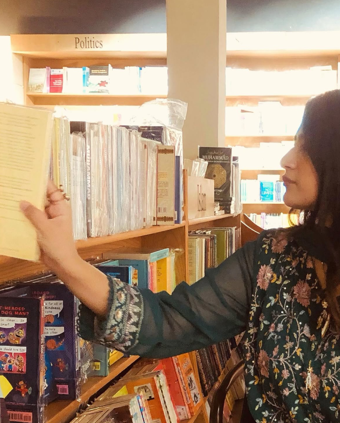 Amna reaching for a book on a bookshop shelf